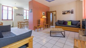 A living room with a sofa, a coffee table, and a TV stand. There is a dining area with chairs and a table. - Gîte - THOIRY - Gîte (THOIRY)