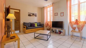 A living room with a sofa, TV, and a table. - Gîte - THOIRY - Gîte (THOIRY)