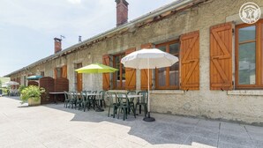 An outdoor seating area with tables and chairs, wooden shutters, and a stone building facade. - Gîte - THOIRY - Gîte (THOIRY)