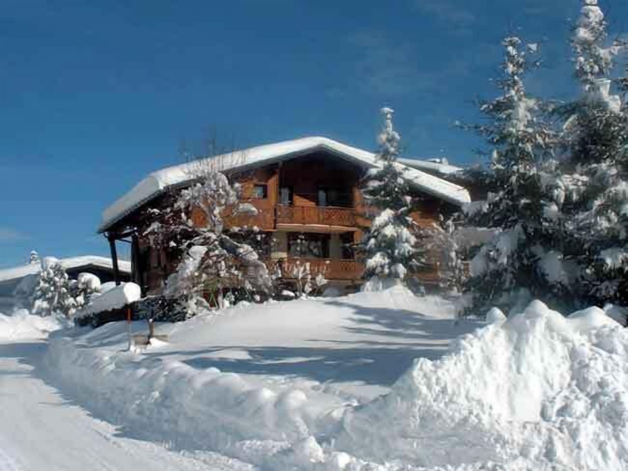 Eine Holzhütte mit Balkon, umgeben von schneebedeckten Bäumen und blauem Himmel.