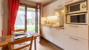 A compact kitchen with white cabinets, a microwave, a coffee maker, and a dining area with a table and chairs. - LACHAT - CHALET LA LICORNE (NOTRE-DAME-DE-BELLECOMBE)