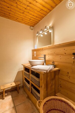 A wooden bathroom with a large sink, a mirror, and shelves with baskets.