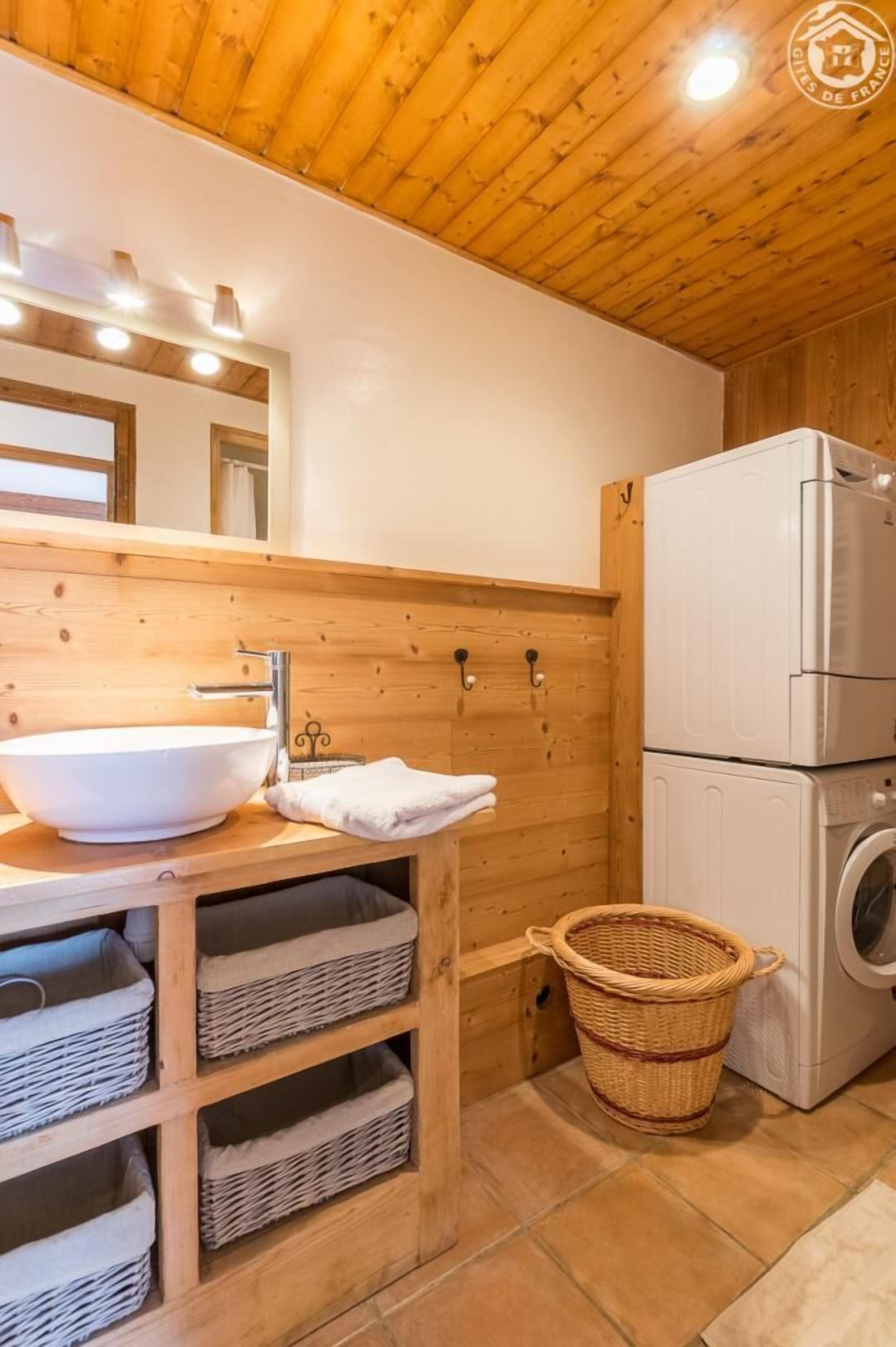 A wooden cabin-style bathroom with a large white sink, a mirror, and a washing machine.