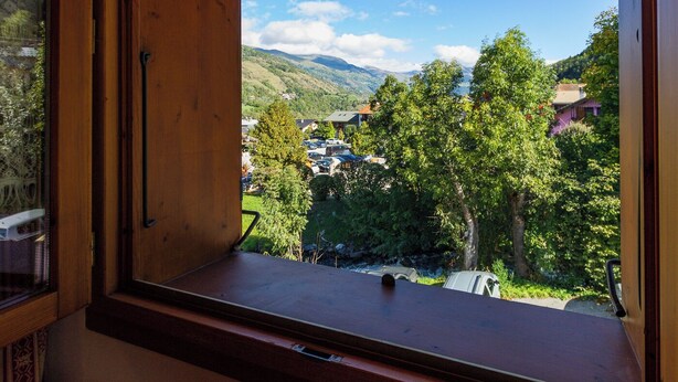 Una finestra con cornice di legno che si affaccia su una valle, case e auto parcheggiate.