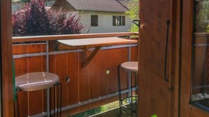 Un balcone in legno con due sgabelli e un tavolo, affacciato su un paesaggio montuoso con case.