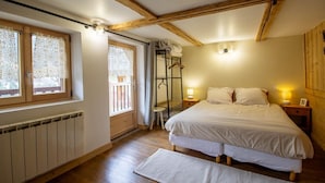 A bedroom with a wooden ceiling, a large bed, two bedside lamps, a radiator, and a window with lace curtains. - LE GRENIER - HAUTELUCE LES SAISIES (HAUTELUCE LES SAISIES)