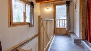 A narrow hallway with wooden railings, a wooden door leading to a balcony, and a window with a lace curtain. - LE GRENIER - HAUTELUCE LES SAISIES (HAUTELUCE LES SAISIES)