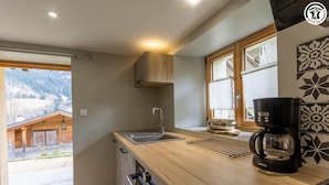 A modern kitchen with a wooden countertop, a coffee maker, and a view of a mountain cabin through the window. - LE GRENIER - HAUTELUCE LES SAISIES (HAUTELUCE LES SAISIES)