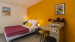 Une chambre d’hôtel avec un lit, un petit bureau avec une chaise, une bouteille de vin et une bande dessinée encadrée accrochée au mur.