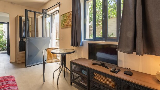 Une pièce comprenant une télévision, une petite table, une chaise, un meuble avec un support pour la télévision et une fenêtre avec des rideaux.