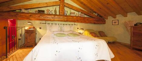A bedroom with a wooden ceiling, a bed with a white bedspread, a nightstand, a dresser, and a small table with a lamp.