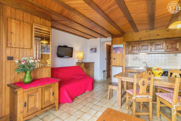 A cozy room with a bed, wooden cabinets, a television, and a dining area with chairs and a table.