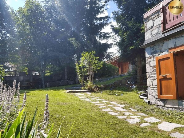 Ein Steinhaus mit einer Holztür, umgeben von einem gepflegten Rasen und einem gepflasterten Weg.