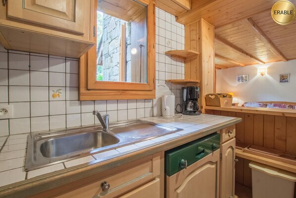 Une cuisine avec des meubles en bois, un évier en acier inoxydable, une machine à café et une fenêtre donnant sur la forêt.