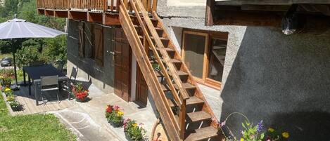 A wooden staircase leading to a balcony with outdoor seating and potted plants.