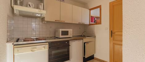 A compact kitchen with a microwave, stove, dishwasher, and oven. There is a small window above the sink and a wooden door to the right.