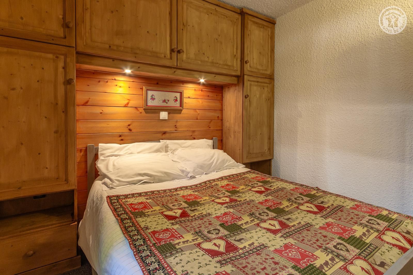 Un dormitorio con paneles de madera, una cama, un colcha y un cuadro en la pared.