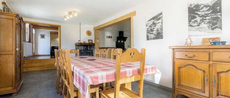 A dining area with a long wooden table and chairs, a wooden cabinet, and a fireplace.