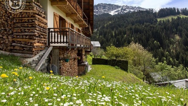 Un bâtiment rustique en bois, doté d’un balcon, entouré d’une prairie verdoyante et s’ouvrant sur un paysage montagneux.