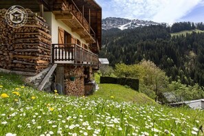 Un bâtiment rustique en bois, doté d’un balcon, entouré d’une prairie verdoyante et s’ouvrant sur un paysage montagneux.