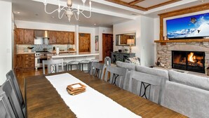 Een ruime woonkamer met een open haard, een eetgedeelte met een lange houten tafel, en een keuken met houten keukenkastjes en een stenen open haard.