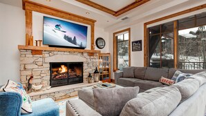 Een gezellige woonkamer met een stenen openhaard, een groot flatscreen televisietoestel erboven en een comfortabele grijze modulaire bank.