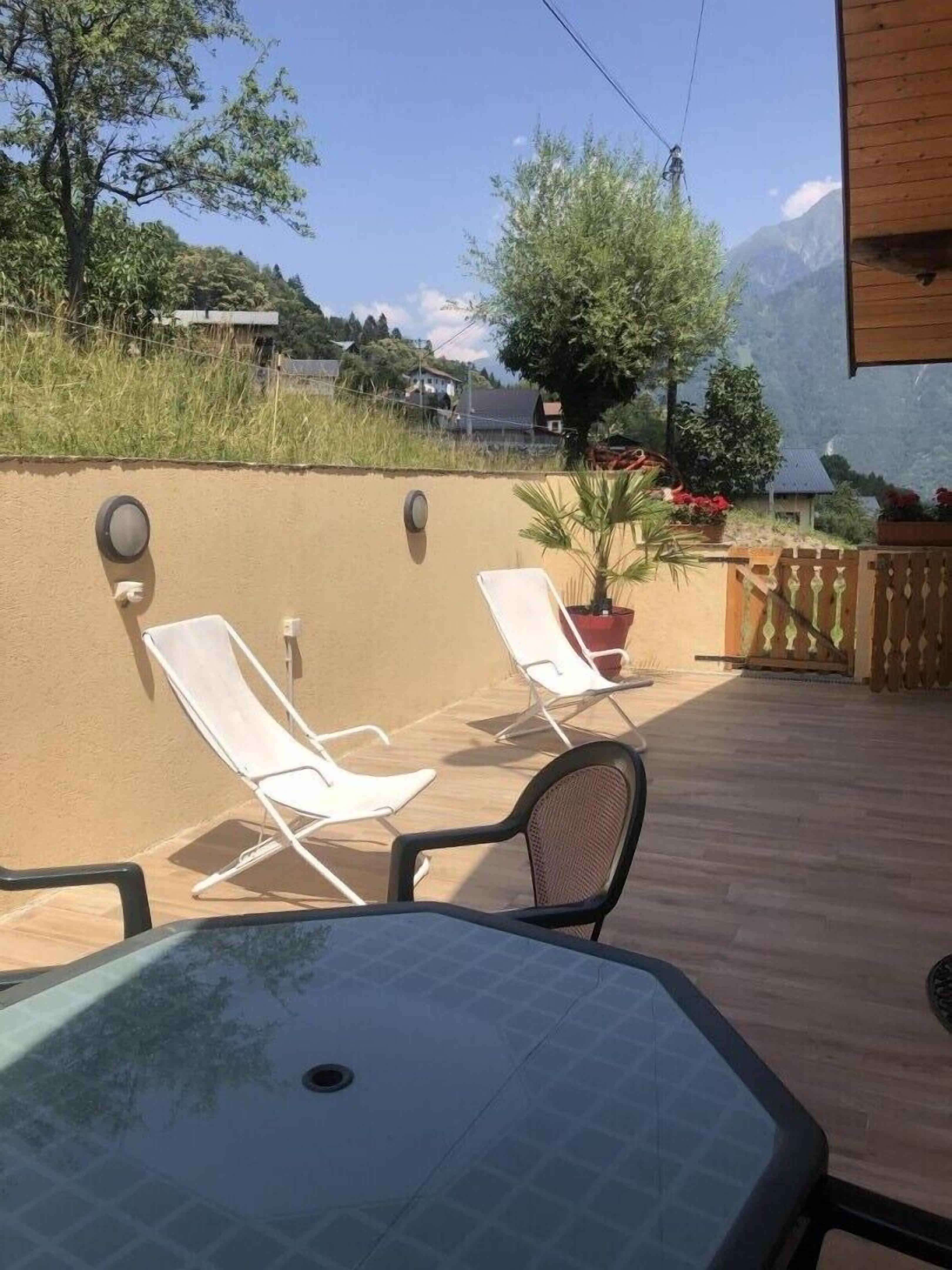 A patio with two white lounge chairs, a table, and a potted plant.