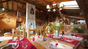 A wooden dining area with tables set for a meal, featuring a rustic interior with exposed beams and a stone wall.
