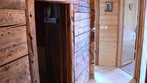 A wooden cabin interior with a wooden door leading to a tiled hallway.