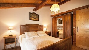 A wooden bed with a headboard, two bedside tables with lamps, a wooden wardrobe, and a wooden ceiling with exposed beams.