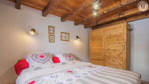 Une chambre avec un plafond en bois, un lit avec une literie à rayures et une armoire en bois.