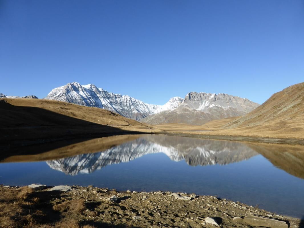 A calm lake with a clear reflection of mountains, surrounded by rocky terrain.