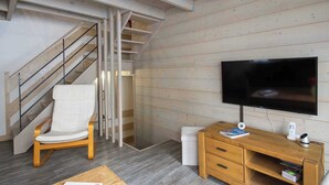 Un salon moderne avec un escalier en bois, un téléviseur à écran plat, un meuble en bois et une chaise blanche.
