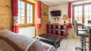 Et hyggeligt værelse med sofa, fjernsyn, en rød hylde og et spisebord.