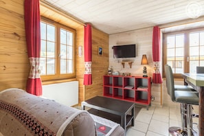 Ein gemütliches Zimmer mit einer Couch, einem Fernseher, einem roten Regal und einem Esstisch.