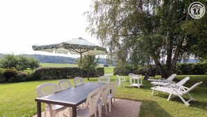 Ein Essbereich im Freien mit Tisch und Stühlen, umgeben von viel Grün und Blick auf die Landschaft.