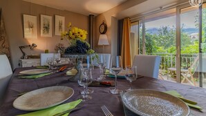 A dining area with a table set for a meal, a vase with flowers, and a view of greenery outside.