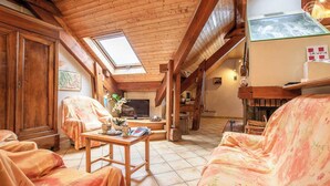 A cozy living room with wooden beams, a TV, and a fireplace.