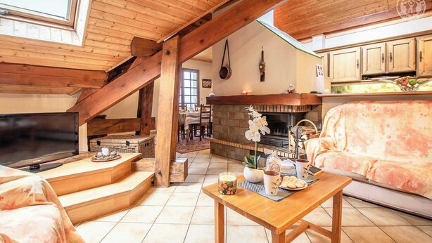 A cozy living room with a fireplace, wooden beams, a TV, and a sofa.