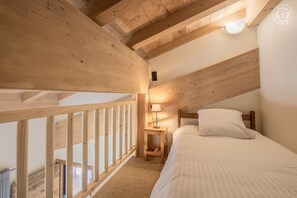 A bedroom with a wooden ceiling, a bed with white bedding, a nightstand with a lamp, and a view through a window. - LE VIEUX MOULIN - LA PARRACHEE (VAL CENIS)