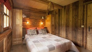 Ein Schlafzimmer einer Holzhütte mit einem Bett, zwei Nachttischlampen und einem Fenster mit Vorhängen.