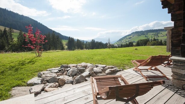 Eine Holzterrasse mit Liegestühlen mit Blick auf ein grünes Feld und Berge.