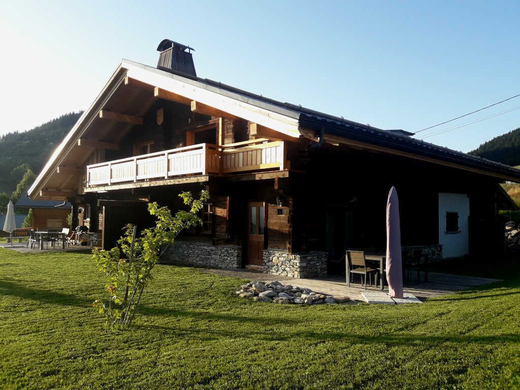 A rustic chalet with a balcony, stone foundation, and a well-maintained lawn.