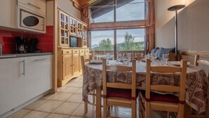A cozy kitchen with wooden cabinets, a built-in microwave, and a dining area with a table set for two. - CRISTAL 4 - HAUTELUCE LES SAISIES (HAUTELUCE LES SAISIES)