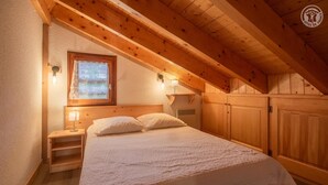 A cozy attic bedroom with a wooden ceiling, a single bed with white linens, a nightstand, a window with a view, and wooden wardrobes. - CRISTAL 4 - HAUTELUCE LES SAISIES (HAUTELUCE LES SAISIES)