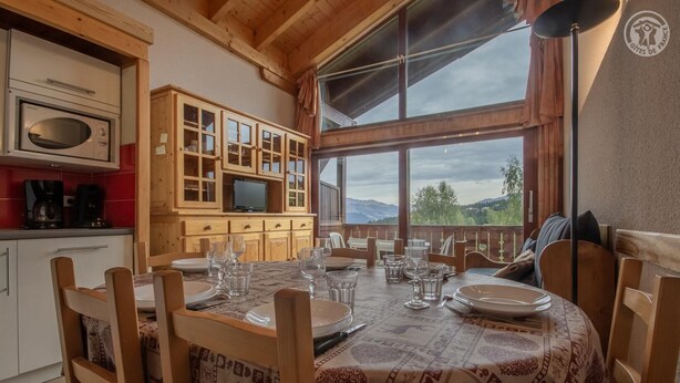 A dining area with a table set for four, wooden cabinets, a microwave, and a television. - CRISTAL 4 - HAUTELUCE LES SAISIES (HAUTELUCE LES SAISIES)