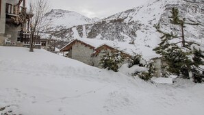 Paisaje nevado de montaña con un edificio de piedra y una cabaña de madera.