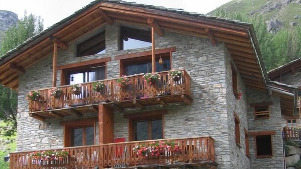 Un edificio de varios pisos de piedra con balcones de madera, un patio cubierto y montañas al fondo.