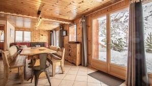 Interior de una cabaña de madera con una mesa de comedor, sillas, un sofá y una televisión.