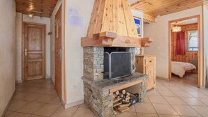 Una habitación acogedora con chimenea de piedra, techo de madera y una puerta que conduce a otra estancia.